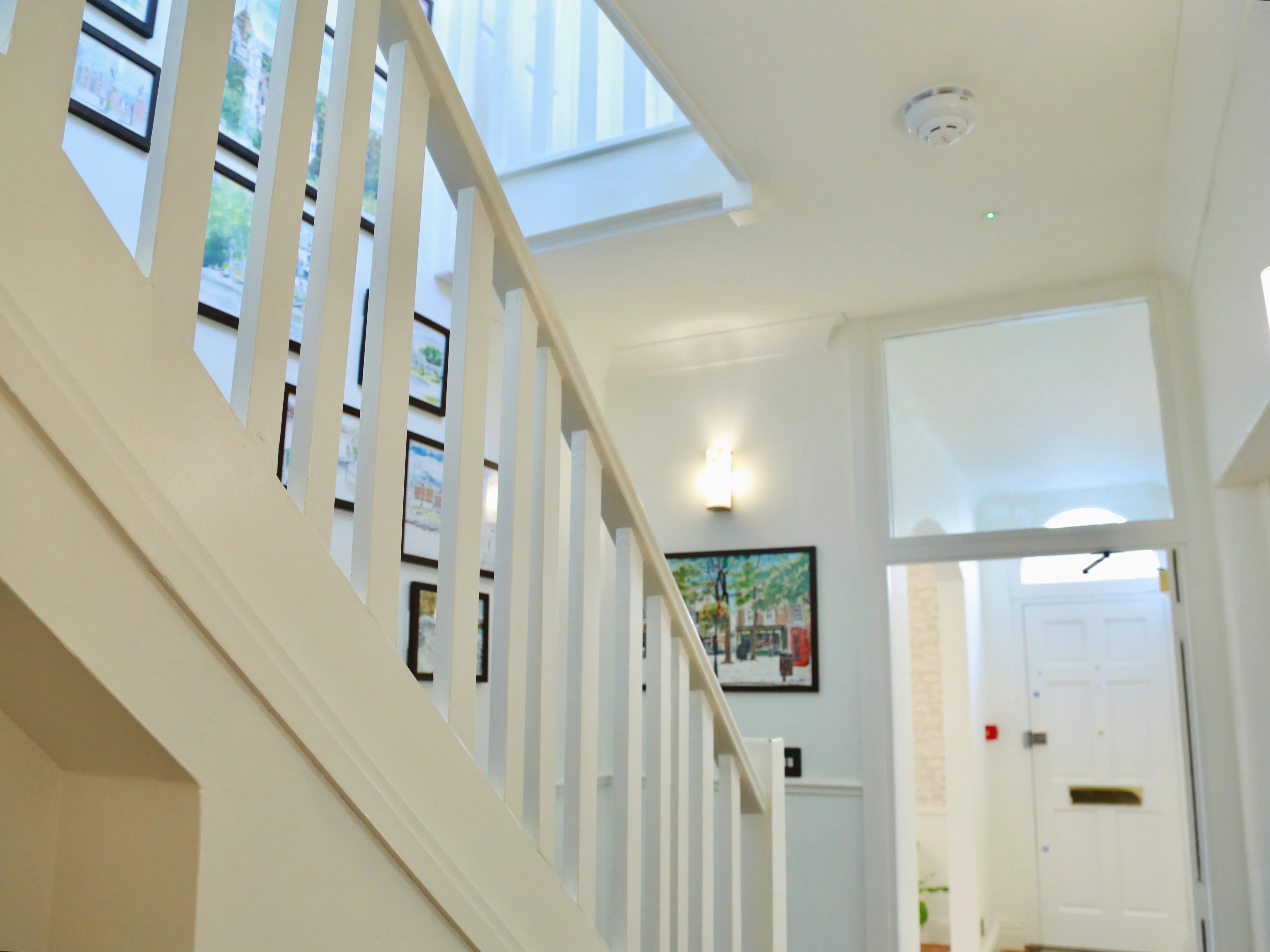 White staircase railing with hallway wall featuring framed artwork and a white front door.