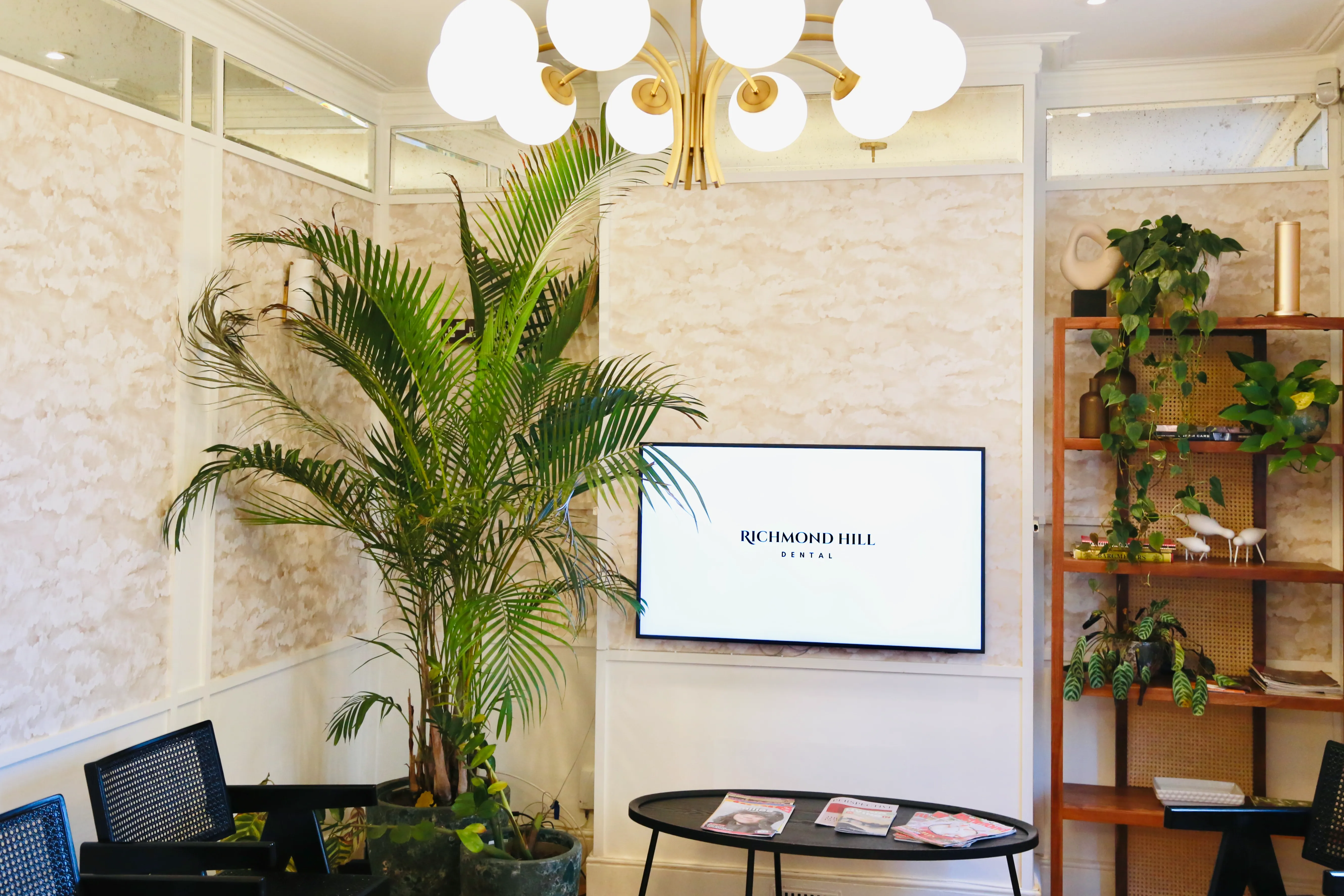 Bright waiting room with large plants, a flat screen reading Richmond Hill Dental, chairs, and a table with magazines.
