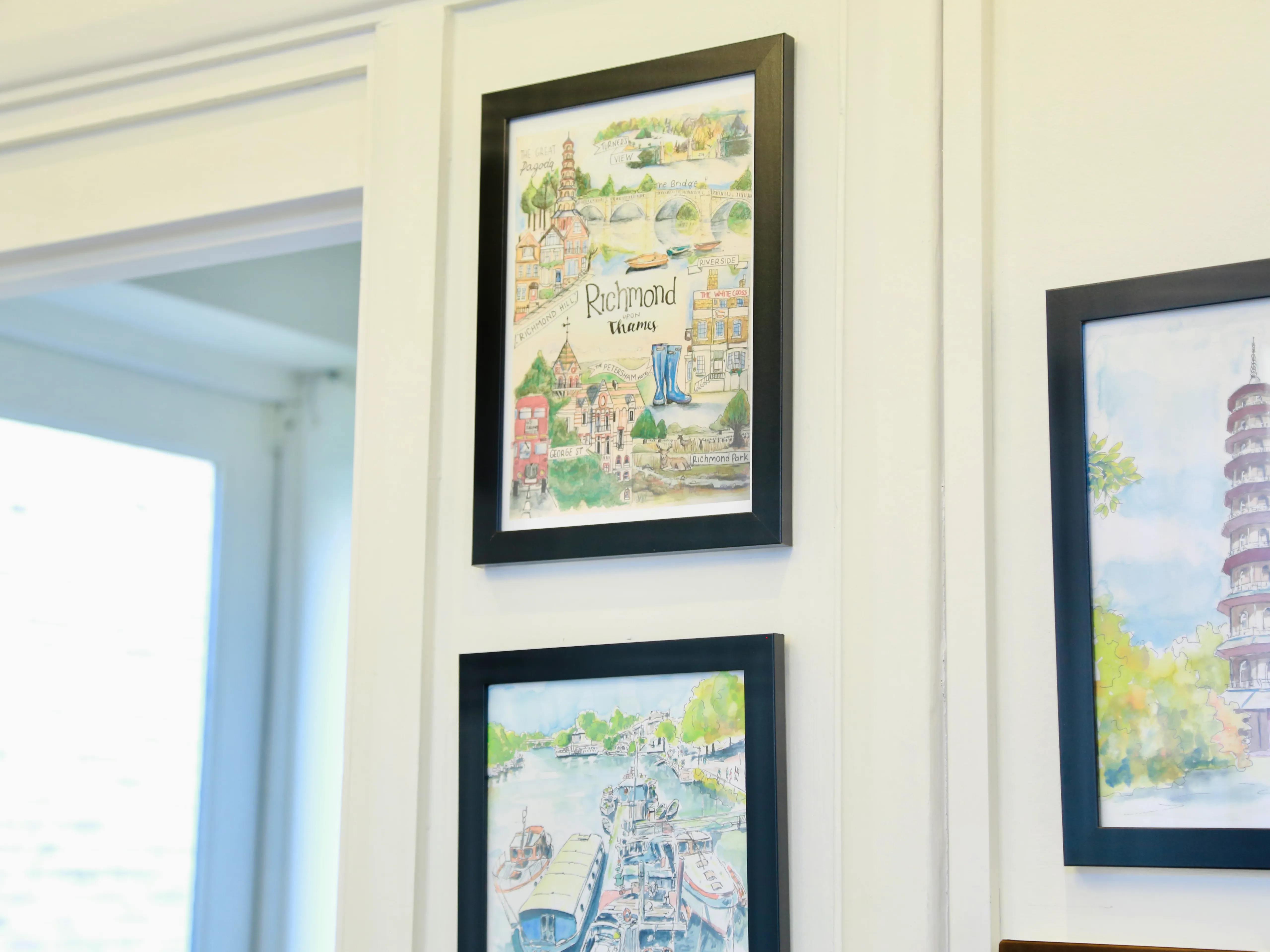 Two framed watercolor paintings on a white wall near a window showing maps and scenes of Richmond upon Thames.