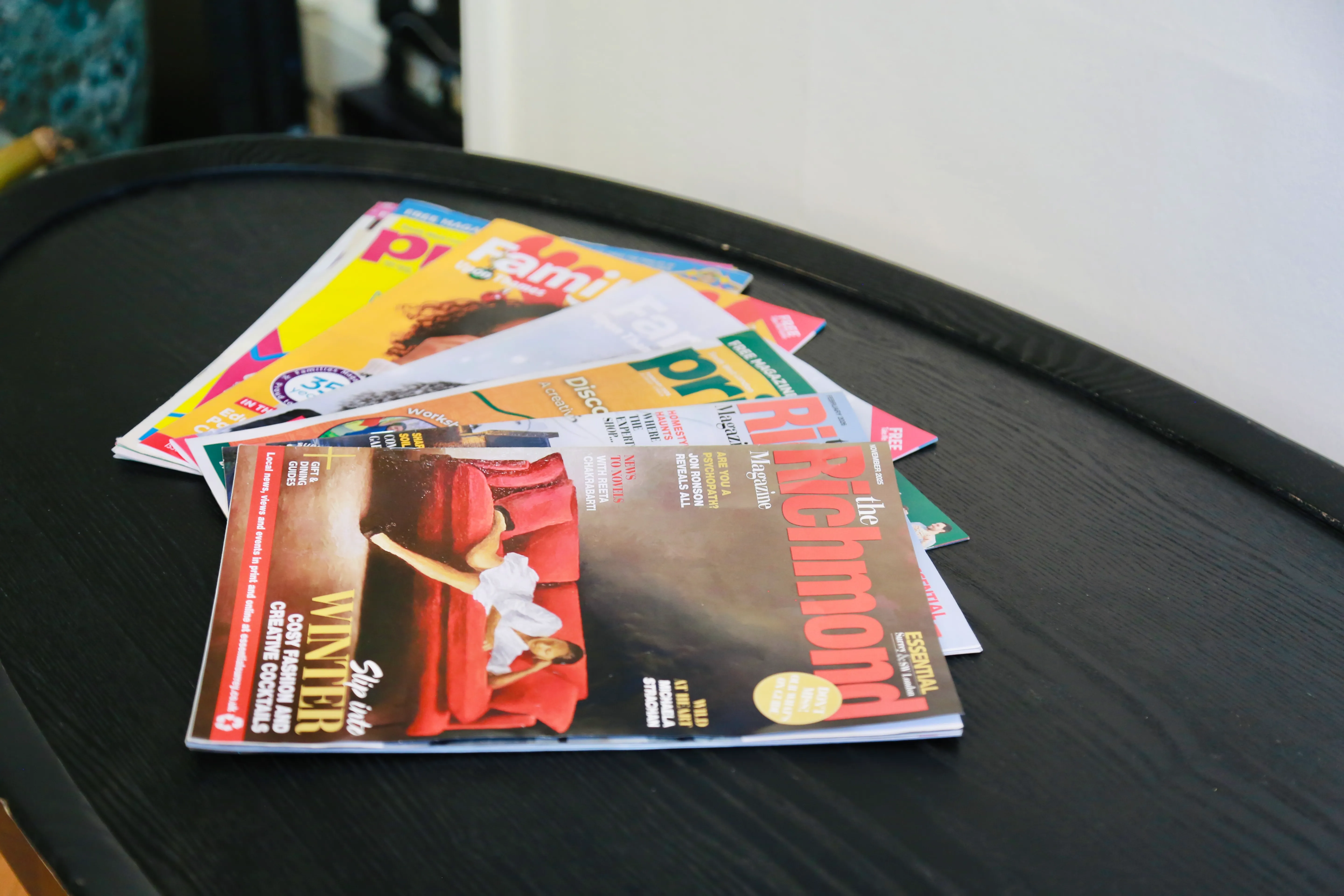 A stack of colorful magazines on a black oval table against a white wall.