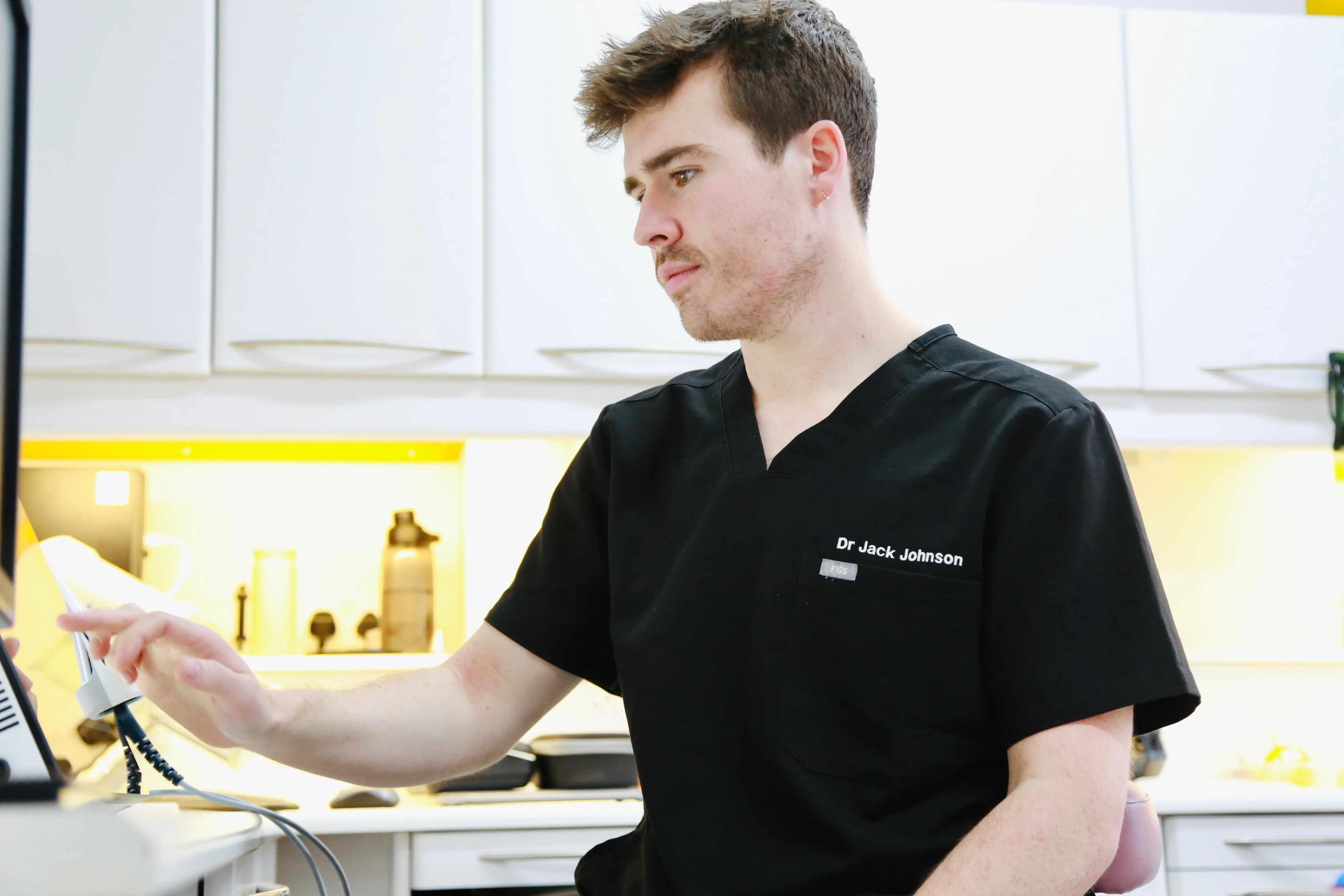 Man in black medical scrubs with name Dr Jack Johnson working on a computer in a clinical setting.