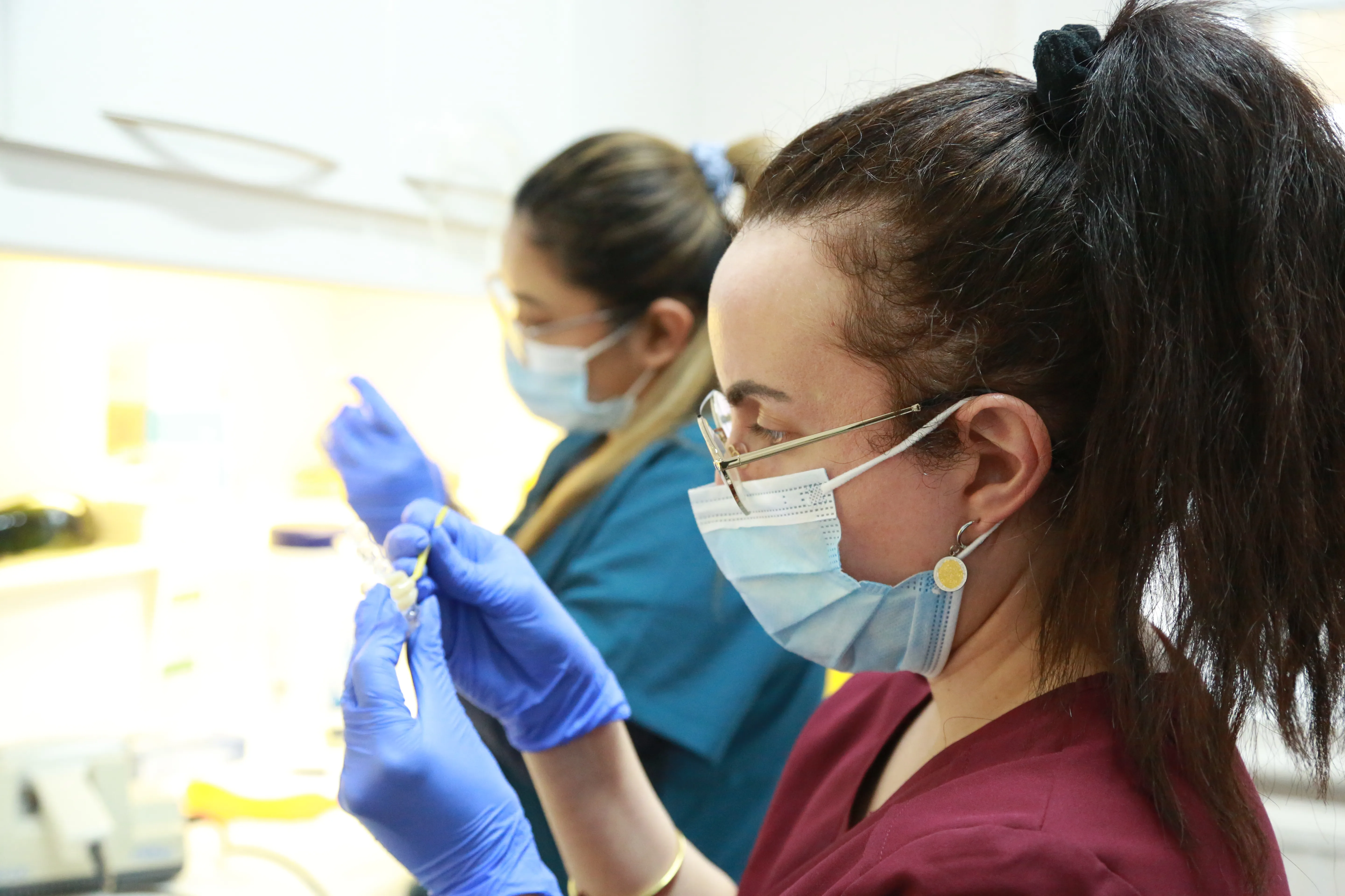 Two female healthcare workers wearing masks and gloves handling medical supplies in a clinical setting.