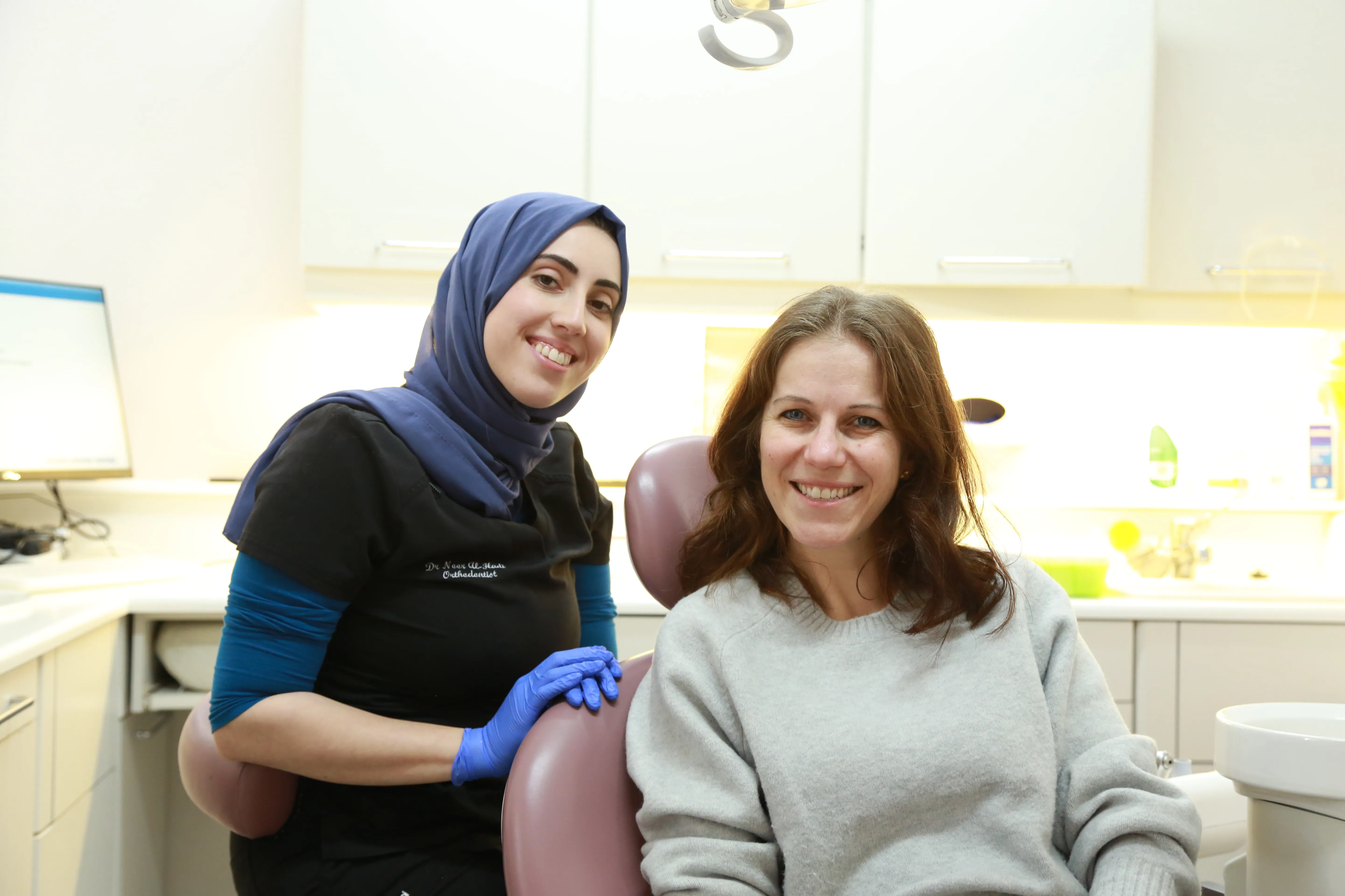 Smiling female orthodontist in a hijab with a patient sitting in a dental chair in a clinic.