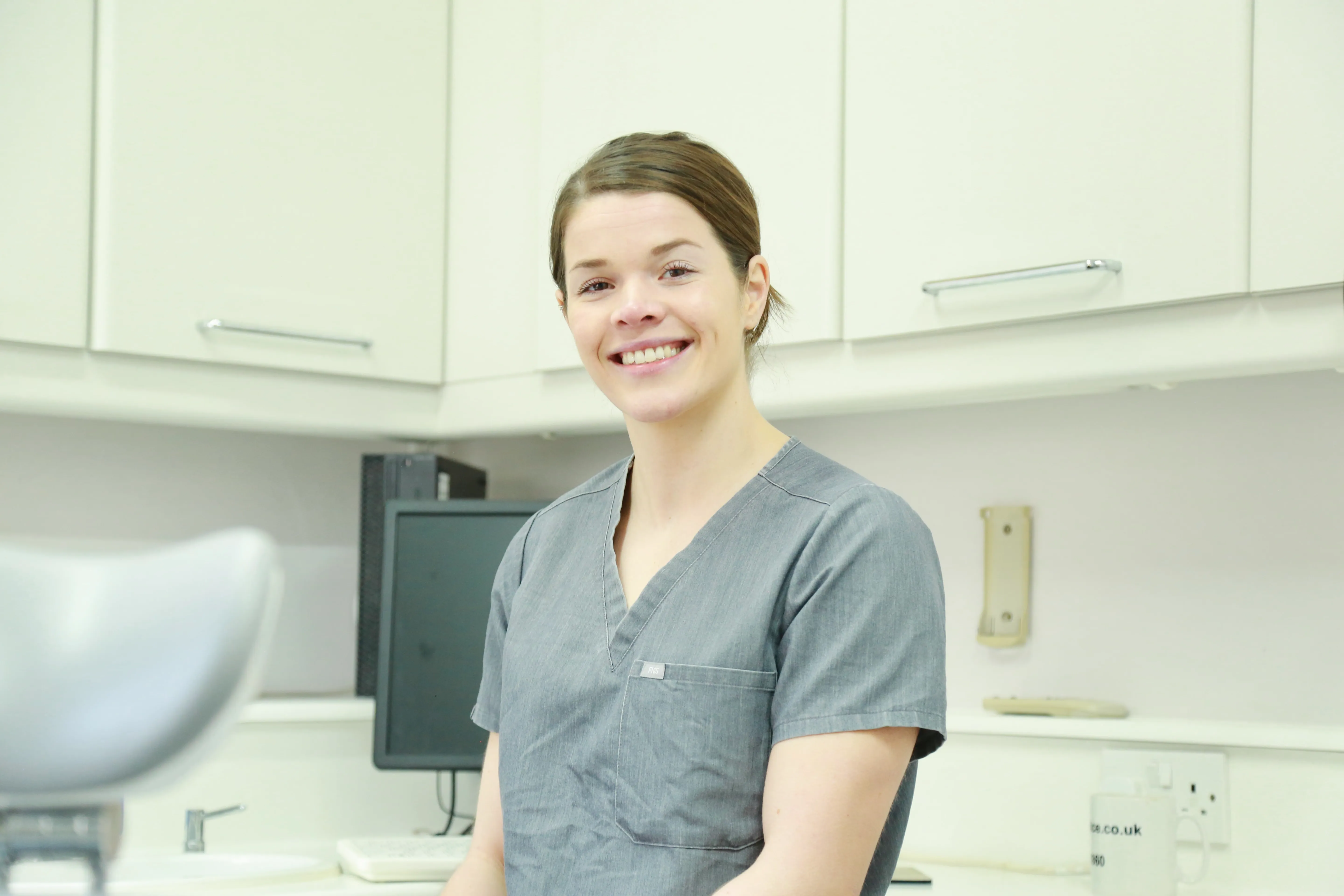 Smiling female healthcare worker in gray scrubs standing in a clean medical office.
