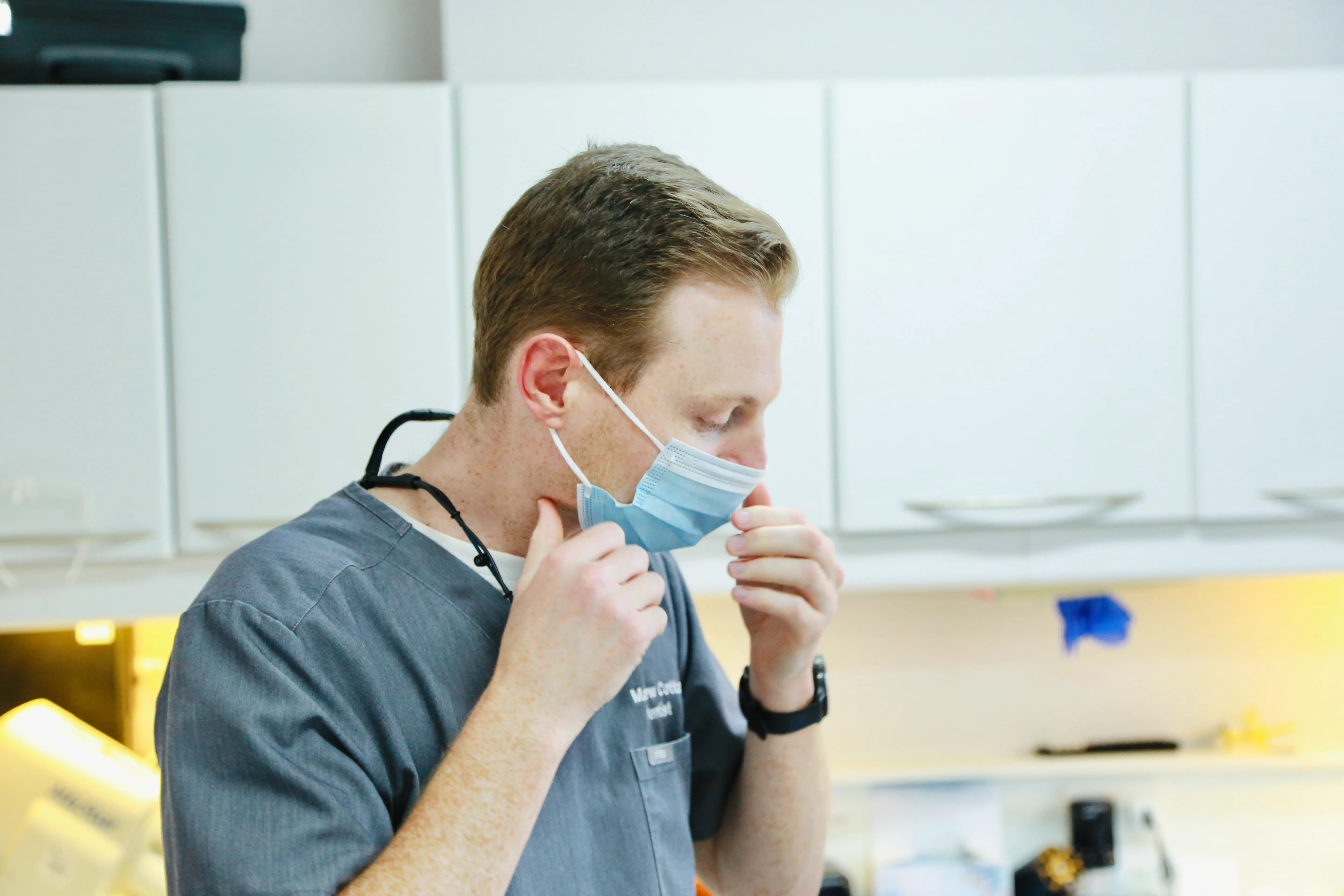 Male healthcare worker removing a blue surgical mask in a medical setting.
