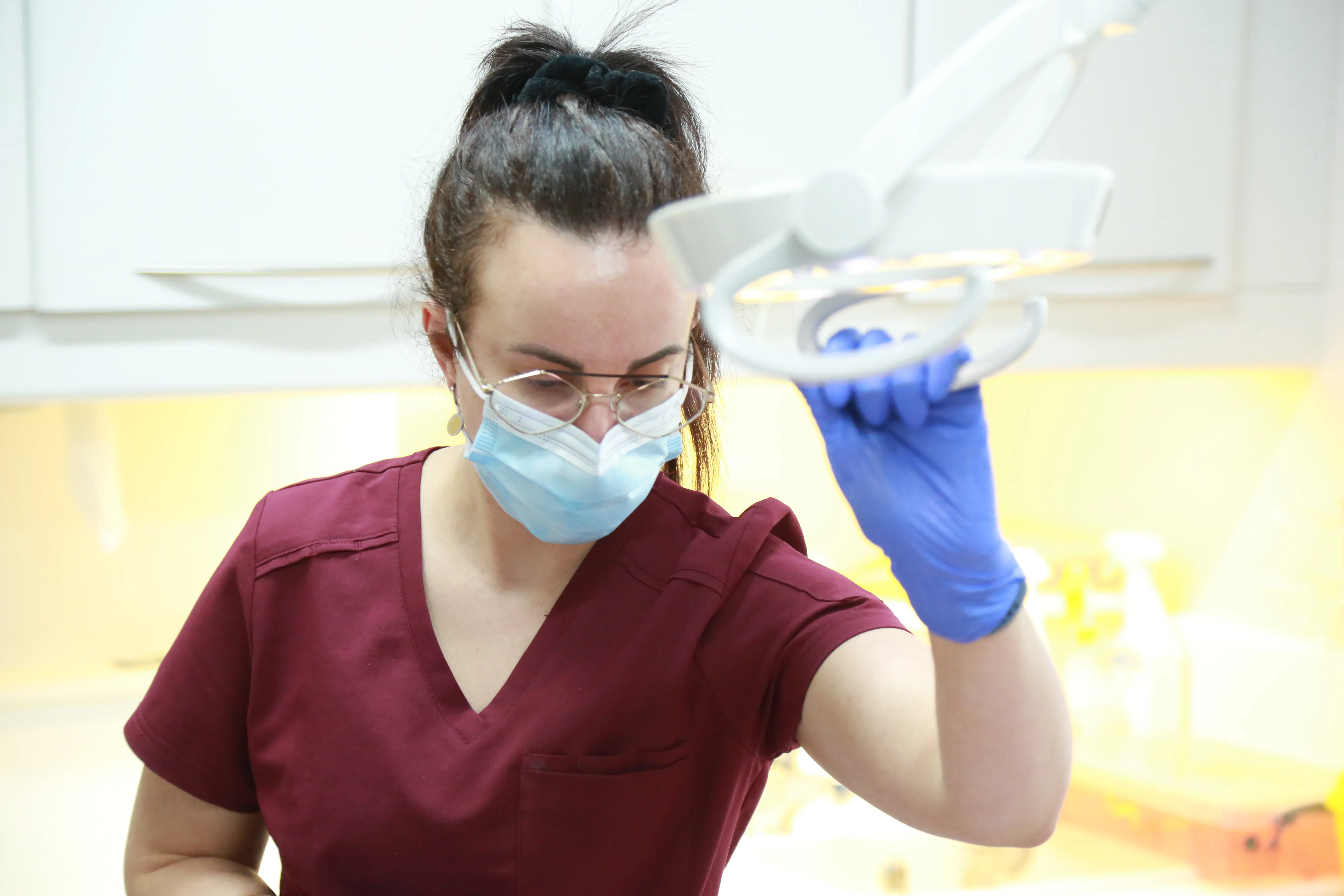 Healthcare worker in a mask and gloves adjusting a medical overhead light in a clinical setting.