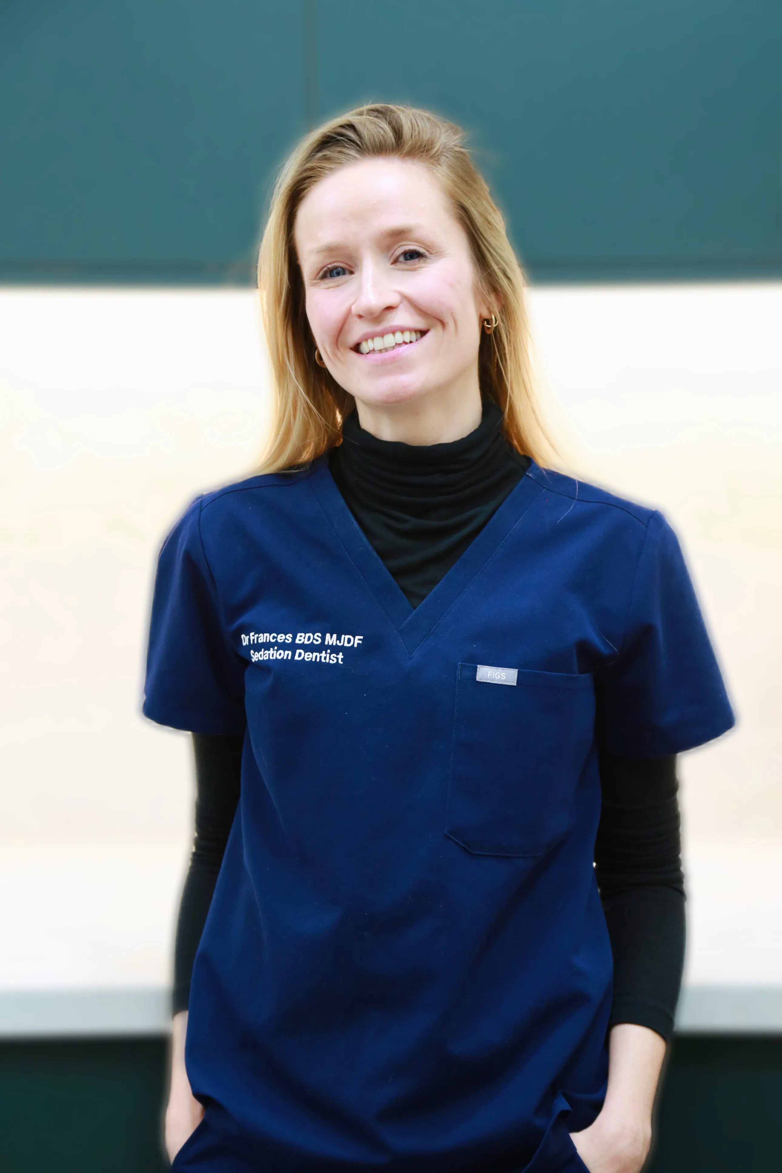 Smiling woman with blonde hair wearing navy scrubs labeled sedation dentist Dr. Frances.