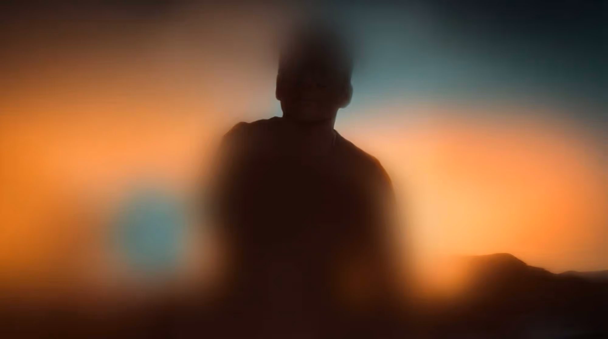 Soft-focus silhouette of a person against a glowing orange and teal sunset