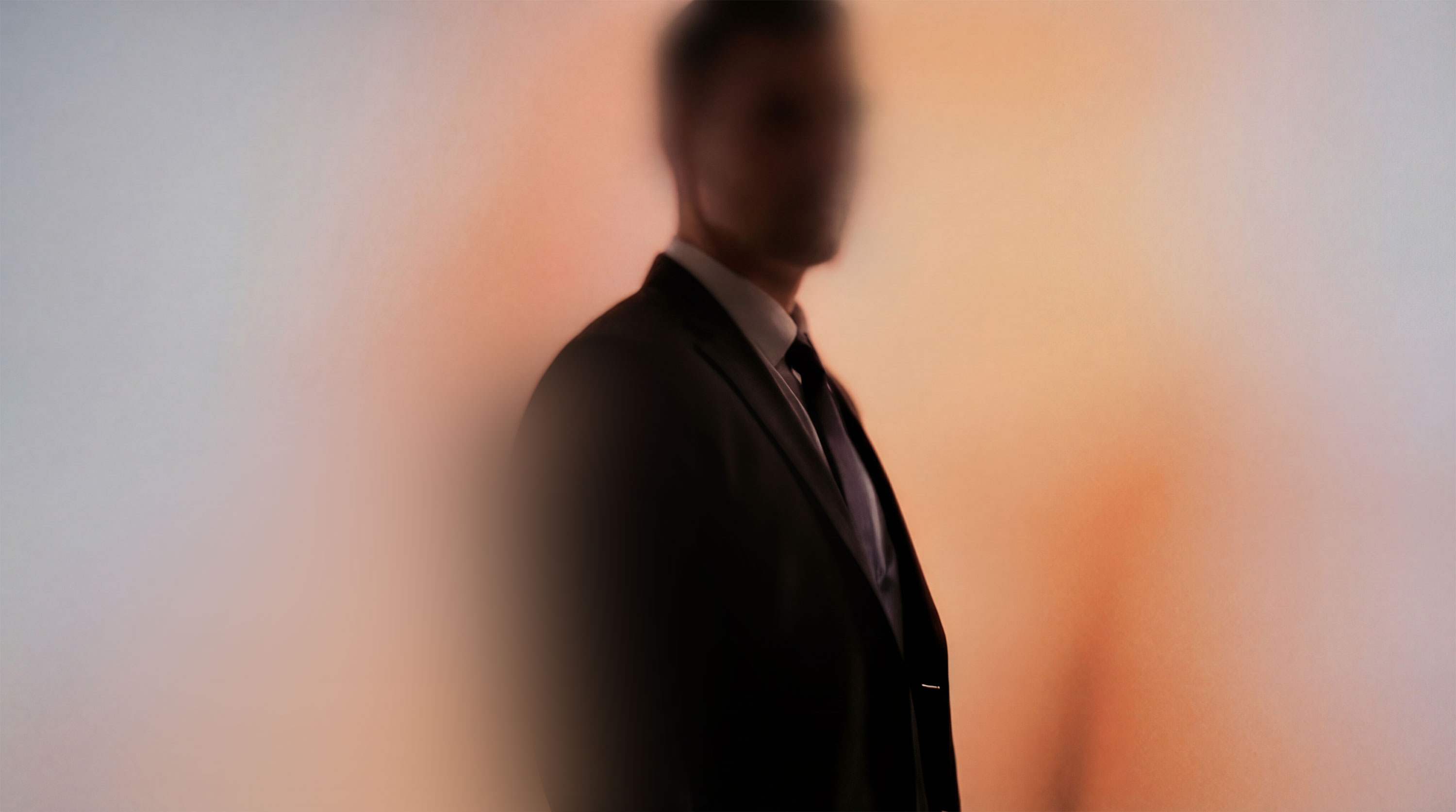 Soft-focus profile of a man in a dark suit and tie against a warm-toned wall