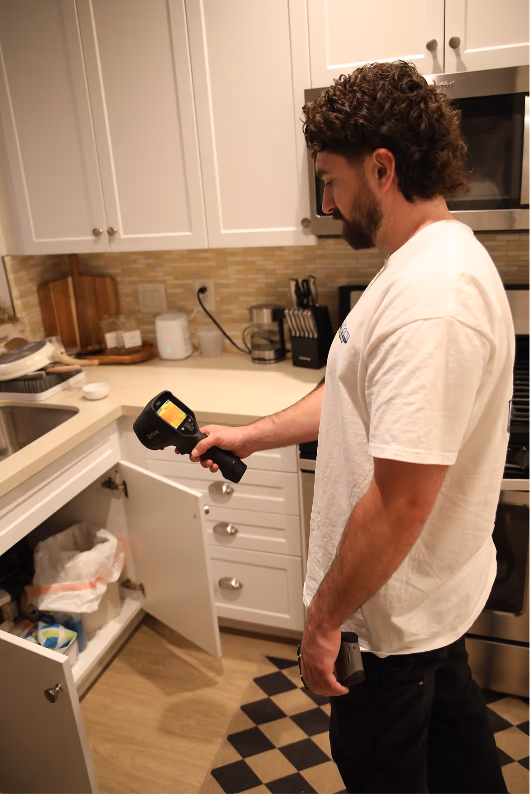 Technician using a thermal camera under a kitchen sink