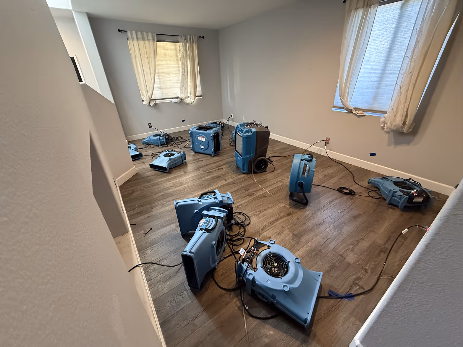 Air movers and a dehumidifier running in a water damaged Orange County room with baseboards removed