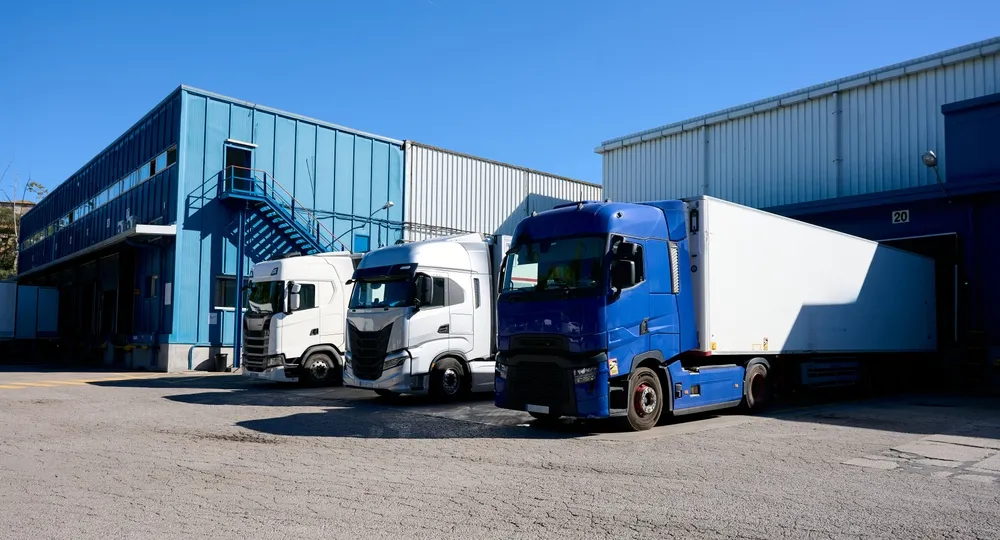 Transport trucks getting loaded at a warehouse. The sun is shining and sky is blue.