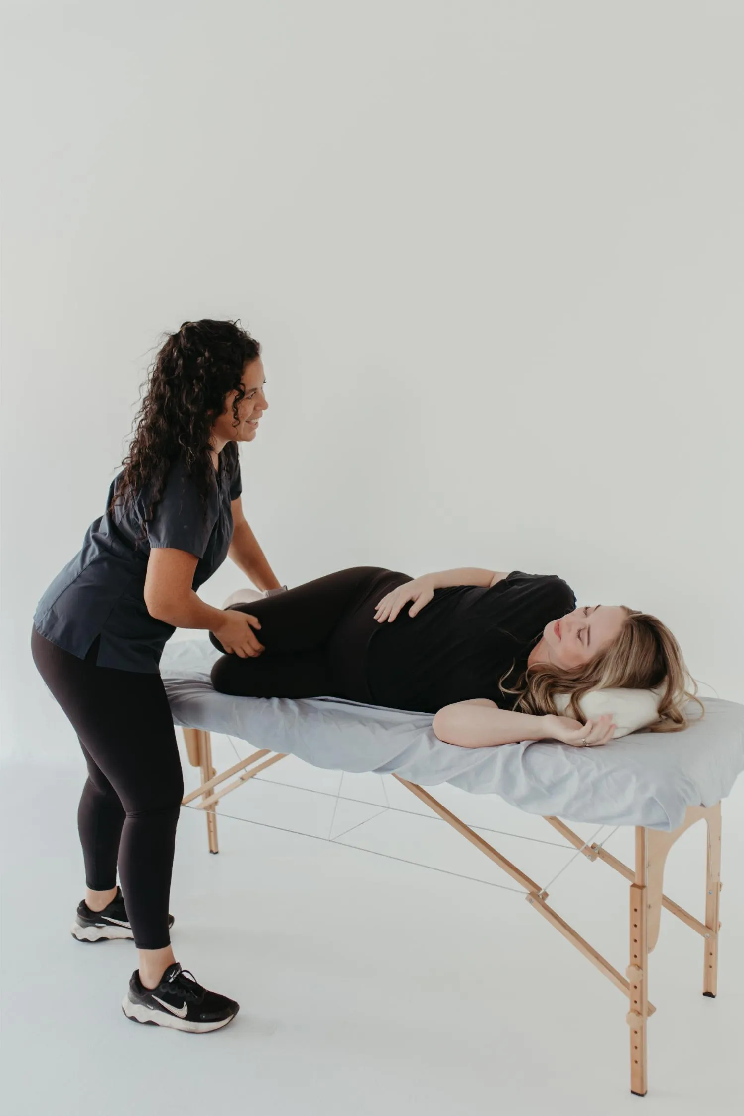 Pregnant woman lying on a massage table receiving a prenatal massage from a therapist.