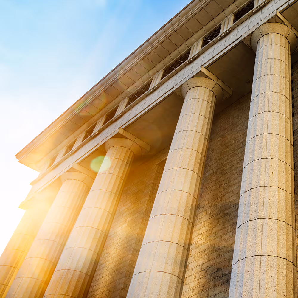 Sunlit classical building with tall stone columns and a blue sky background.