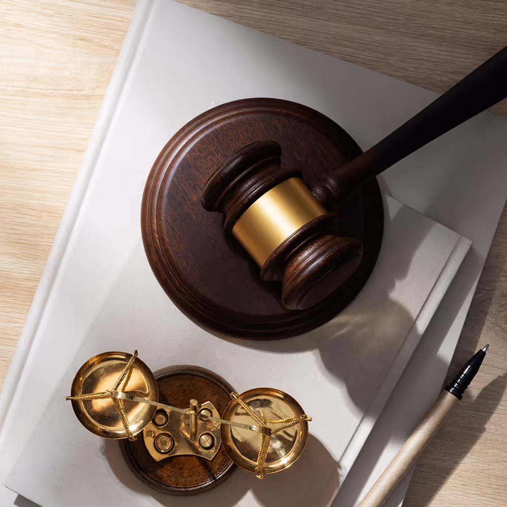 Wooden gavel and golden balance scale on top of stacked white books with a pen nearby.