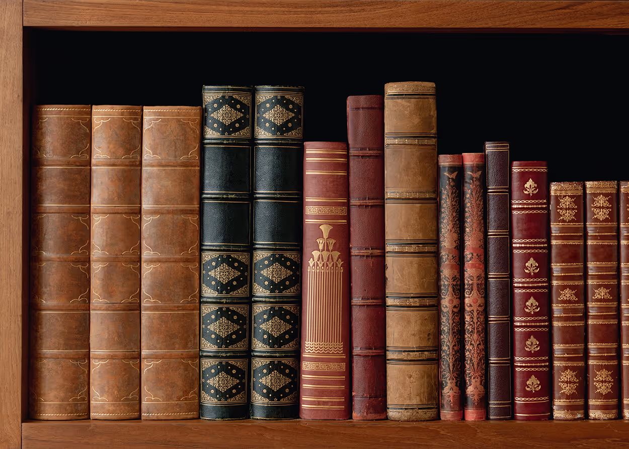 Shelf of antique leather-bound books with intricate gold and red spine designs against black background.