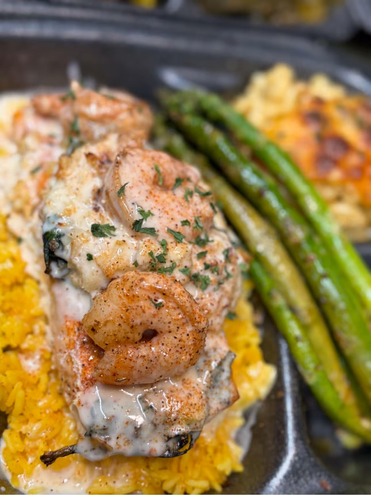 Close-up of a shrimp and creamy sauce dish served on yellow rice with grilled asparagus on the side.