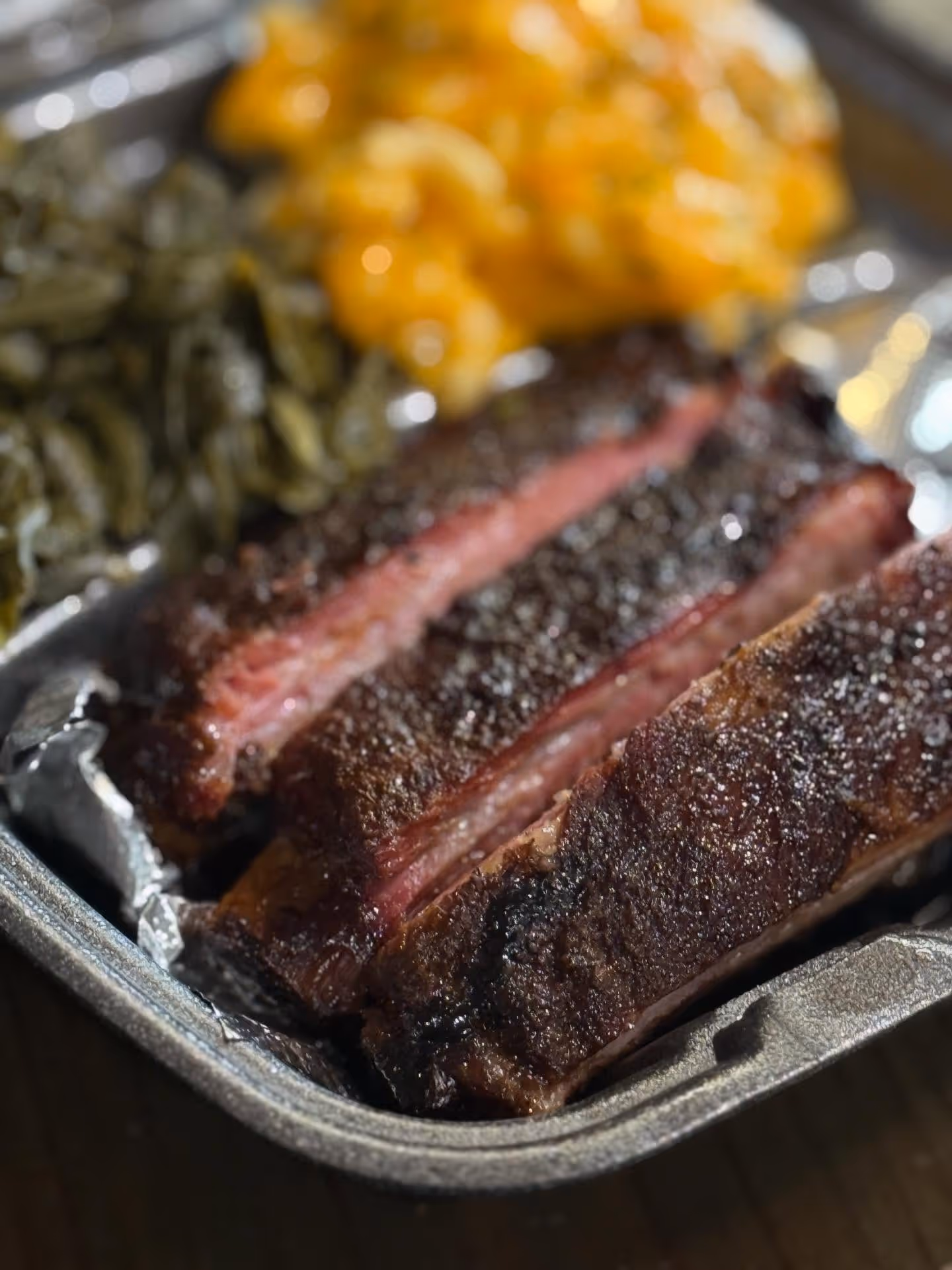Close-up of smoked beef brisket slices in a tray with macaroni and cheese and green beans.