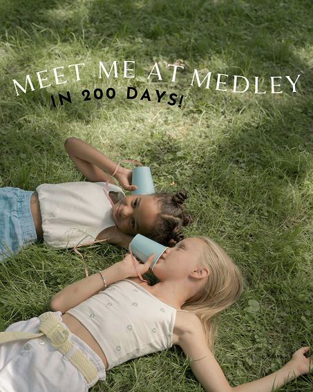 Two children lying on grass outdoors, talking through blue cup string phones.