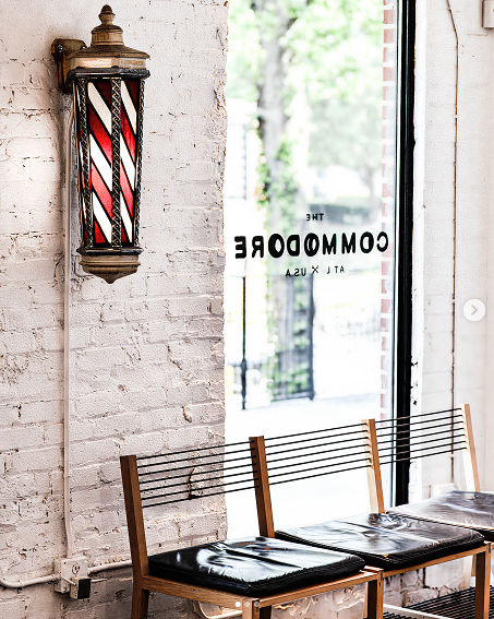 Vintage red, white, and black barber pole light fixture on white brick wall above three black chairs.