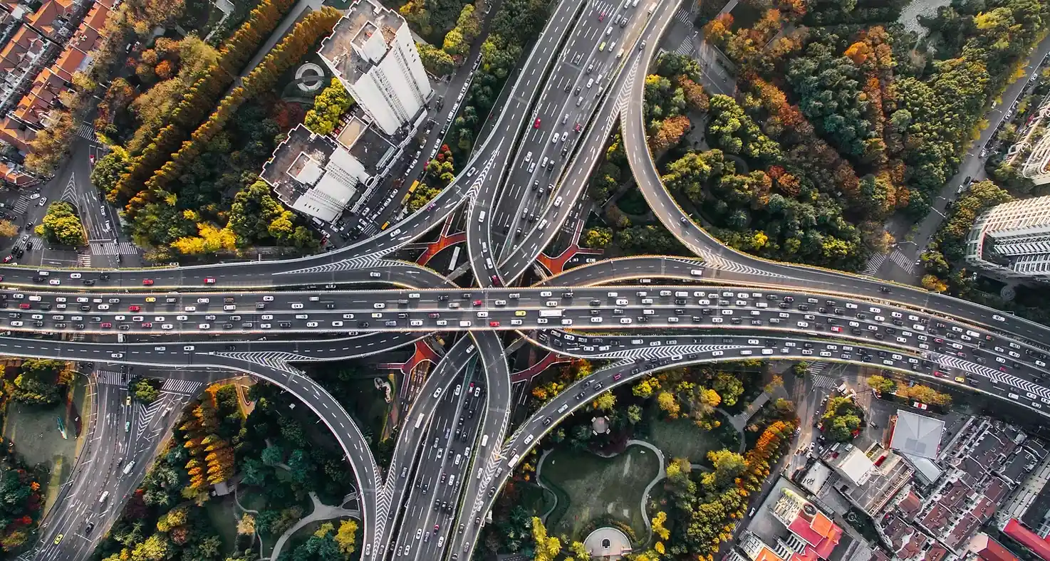Aerial view of a large highway interchange surrounded by trees and buildings with heavy traffic.