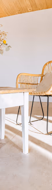 Chaise en rotin avec coussin beige à côté d'une table blanche dans une pièce lumineuse au plafond en bois.