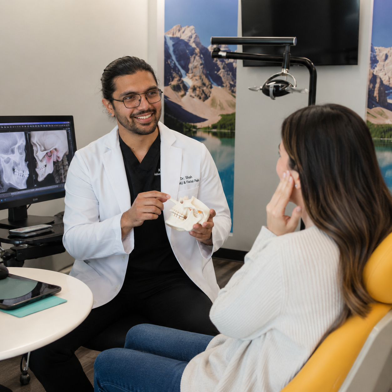 Dr. Karnik Shah holding a jaw anatomy model and explaining TMJ to a female patient with a 3D jaw scan visible on a monitor at Comfydent Smiles in Bee Cave, TX.