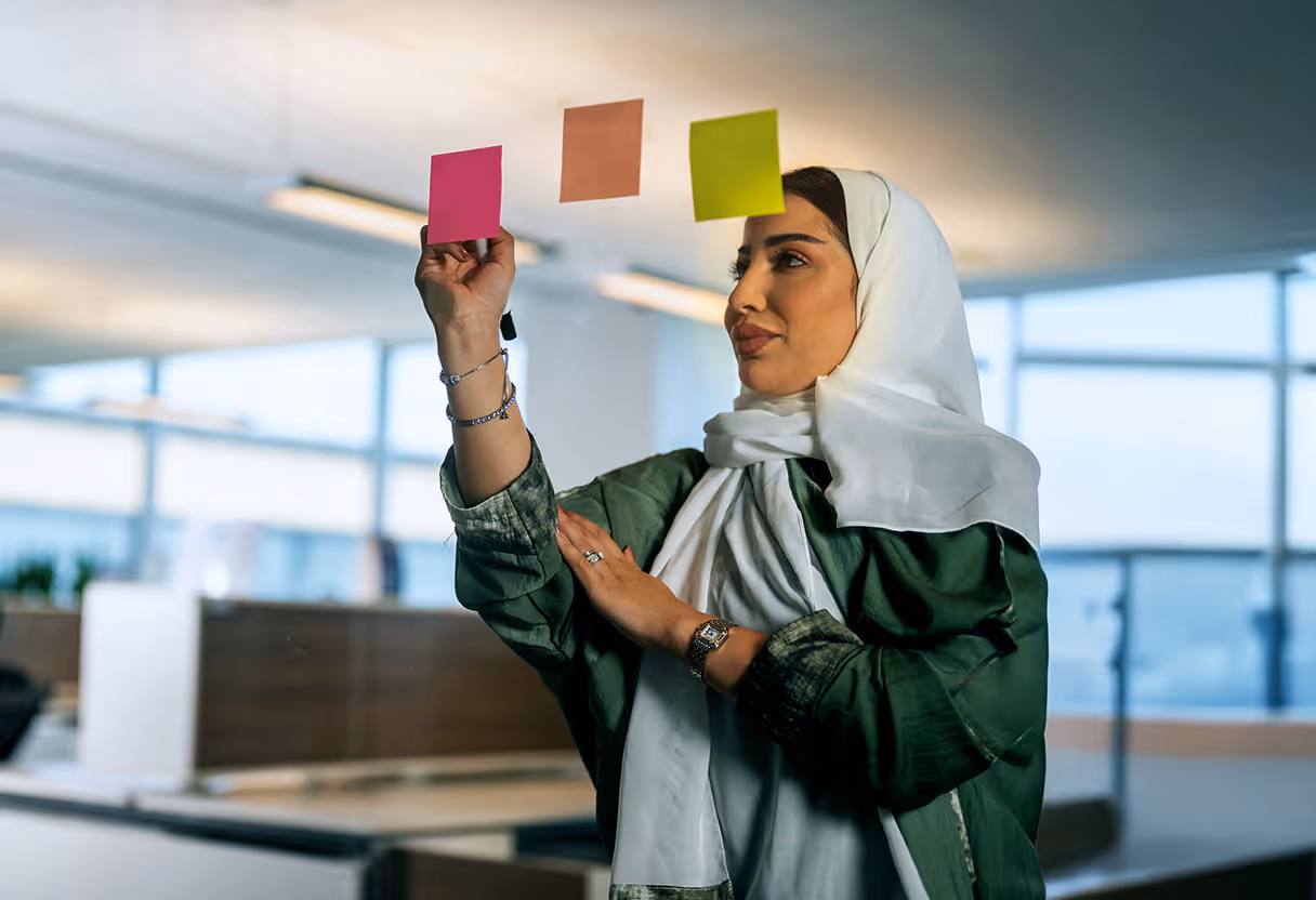امرأة ترتدي الحجاب تضع ملصقات ملونة على زجاج في مكتب حديث.