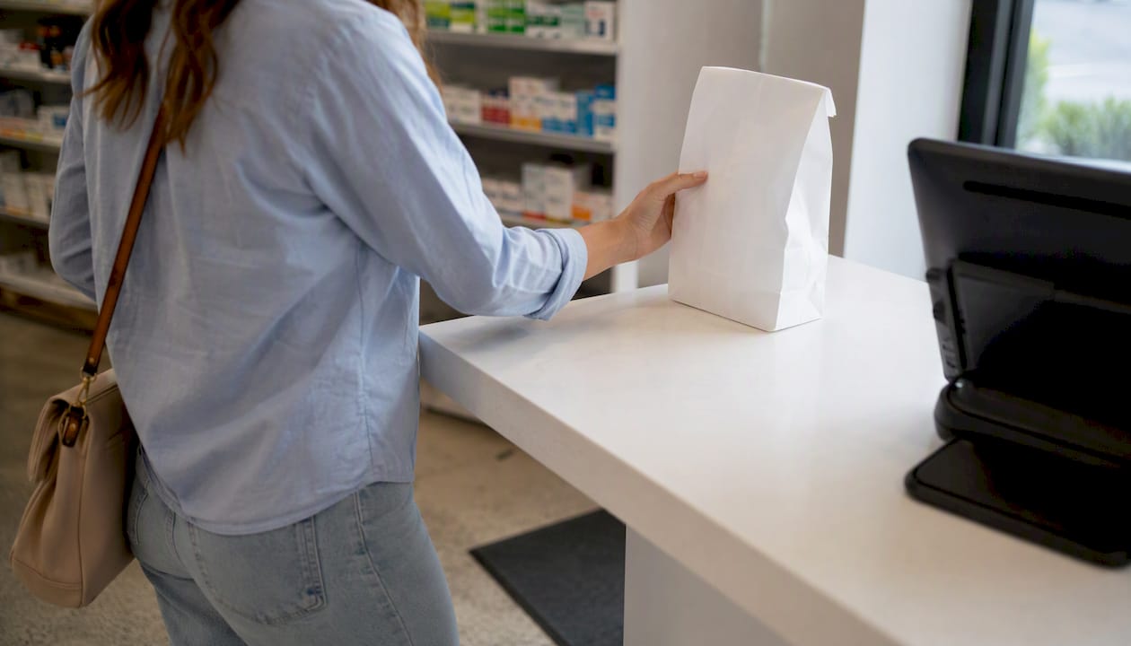 Customer hand receiving prescription at pharmacy pickup counter