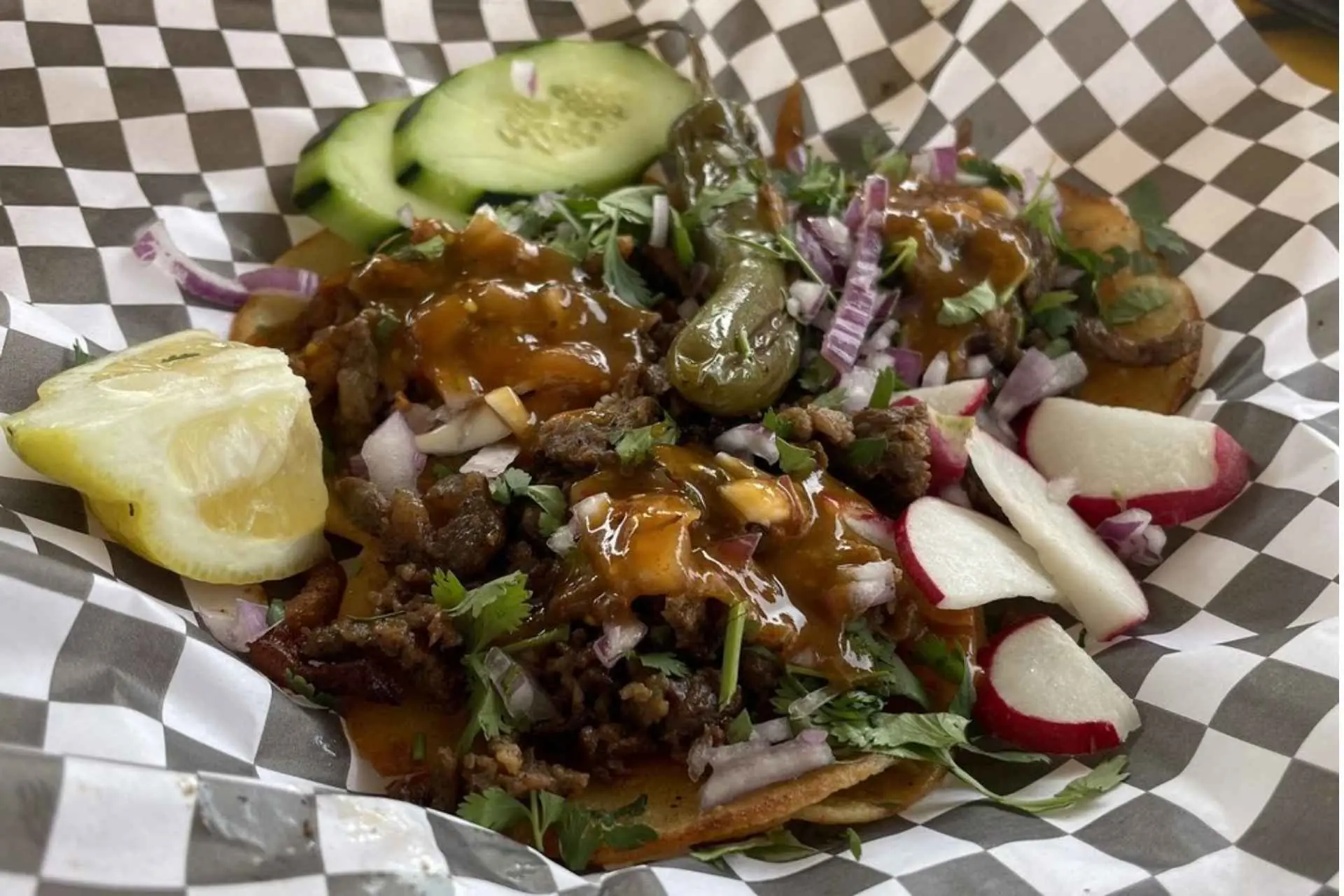 Carne asada tacos topped with onion, cilantro, and salsa, served with cucumber, radish, and lemon at Taco Joe's in Bakersfield