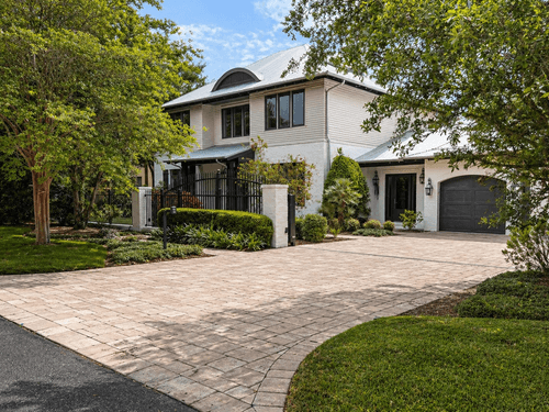 Two-story house with light-colored exterior, metal roof, gated front yard, and paved driveway.