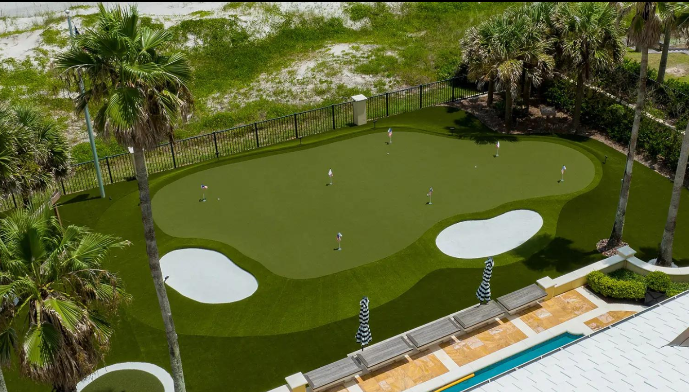 A golf putting green with multiple holes, surrounded by palm trees and benches outdoors.