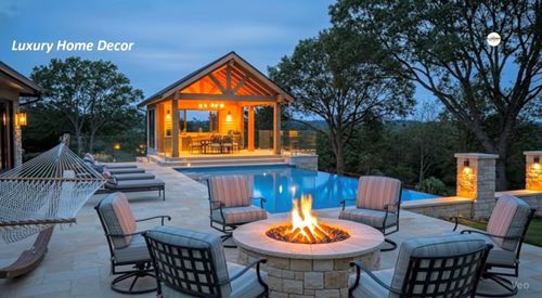 Outdoor patio with fire pit, cushioned chairs, pool, hammock, and a lit wooden gazebo at dusk.