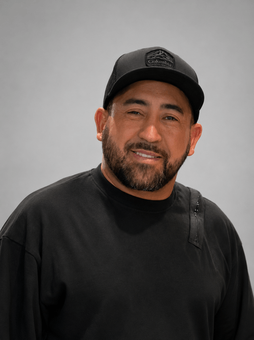 Smiling man with beard wearing a black Columbia cap and black shirt against a gray background.