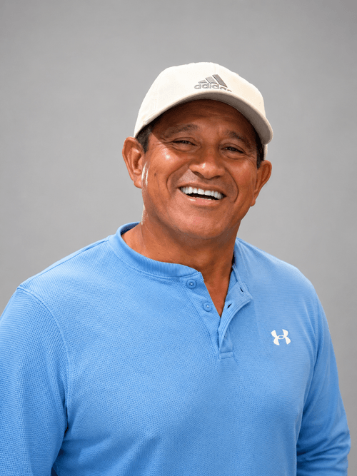Smiling man wearing a white Adidas cap and blue Under Armour shirt against a gray background.