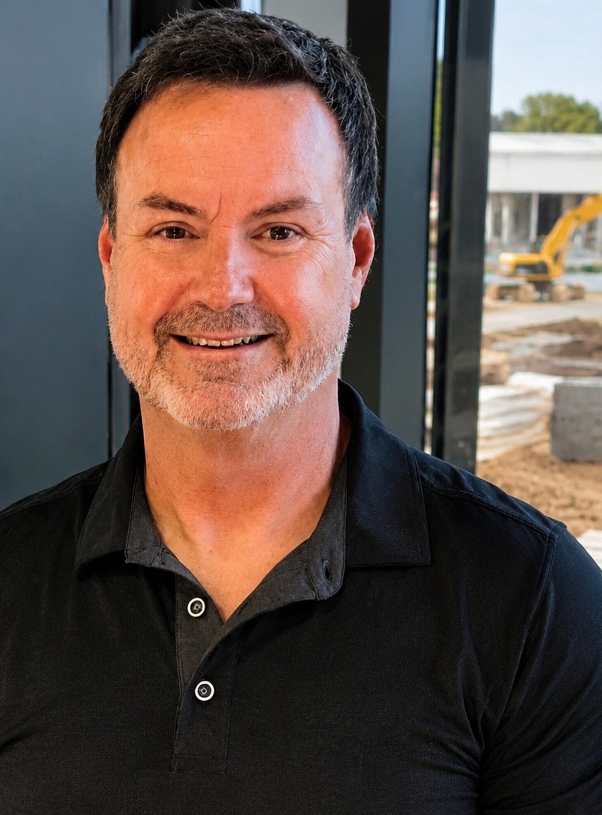 Smiling middle-aged man with short dark hair and beard wearing a black polo shirt.