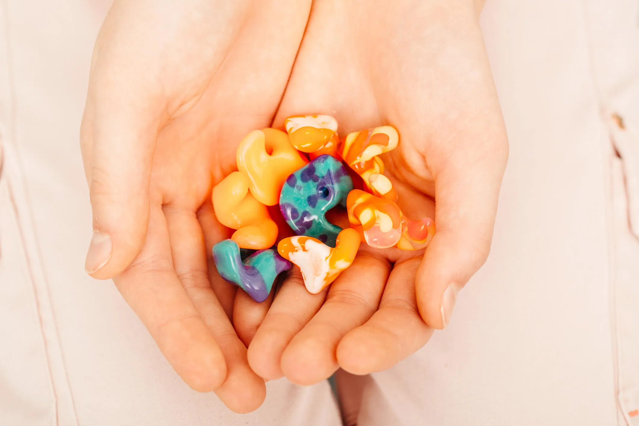Close-up of hands holding colorful molded earplugs in various shapes and patterns.