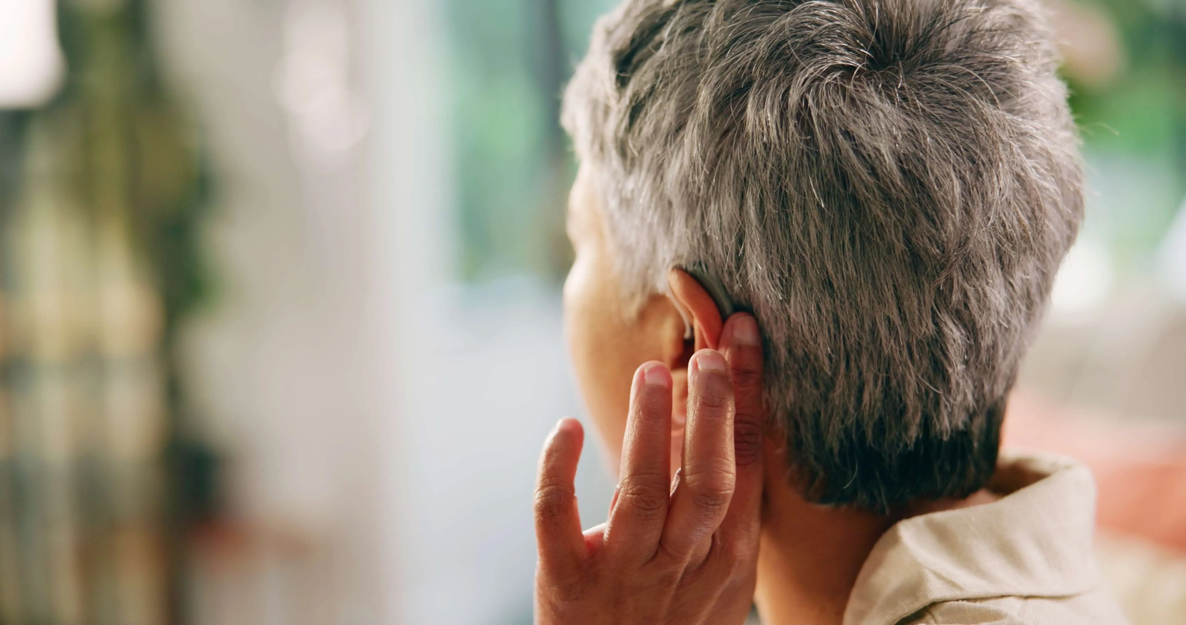 Person with short gray hair adjusting a hearing aid behind their ear.