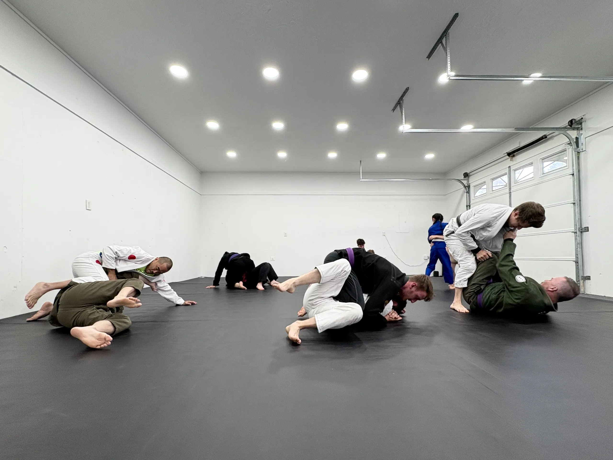 Several pairs practicing Brazilian Jiu-Jitsu on mats in a bright, spacious training room.