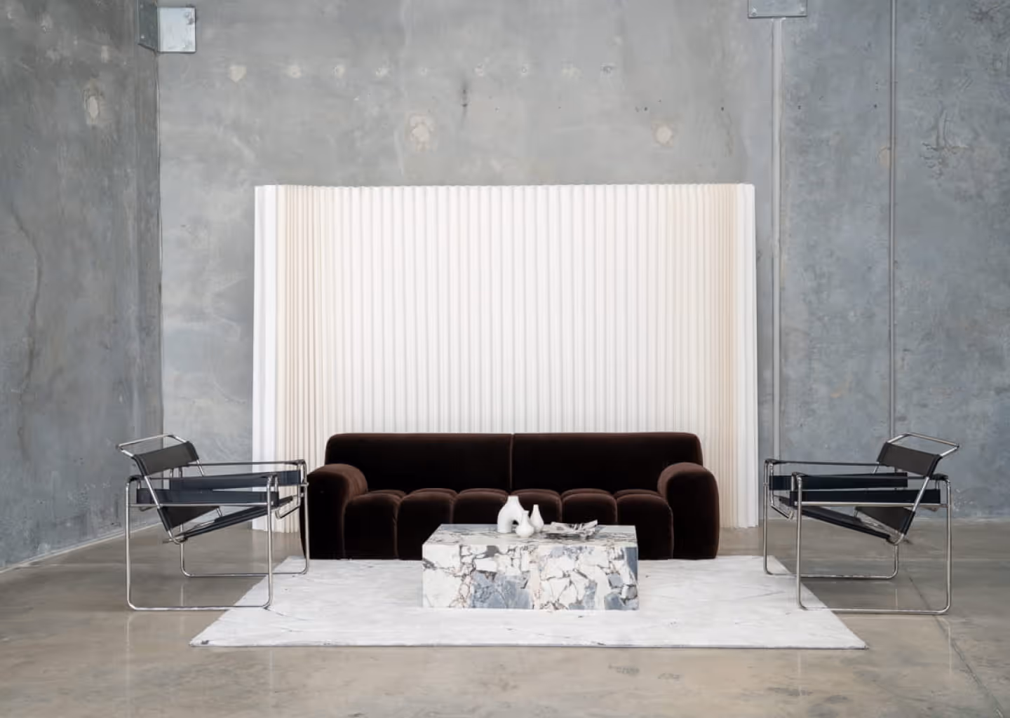 BLANK Studio with dark sofa, two metal-frame chairs, marble coffee table, and white rug.
