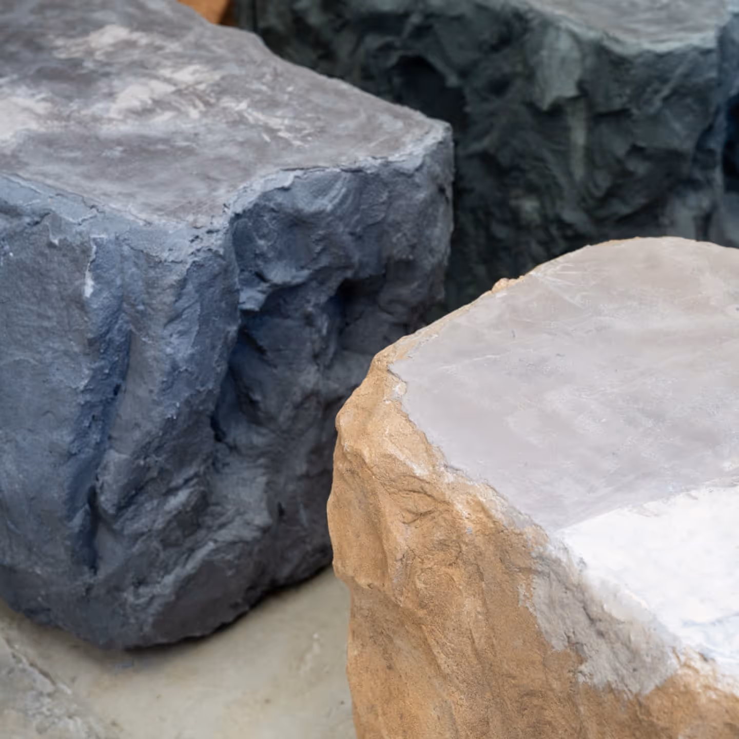 Close-up of textured stone blocks in gray, tan, and dark green colors.