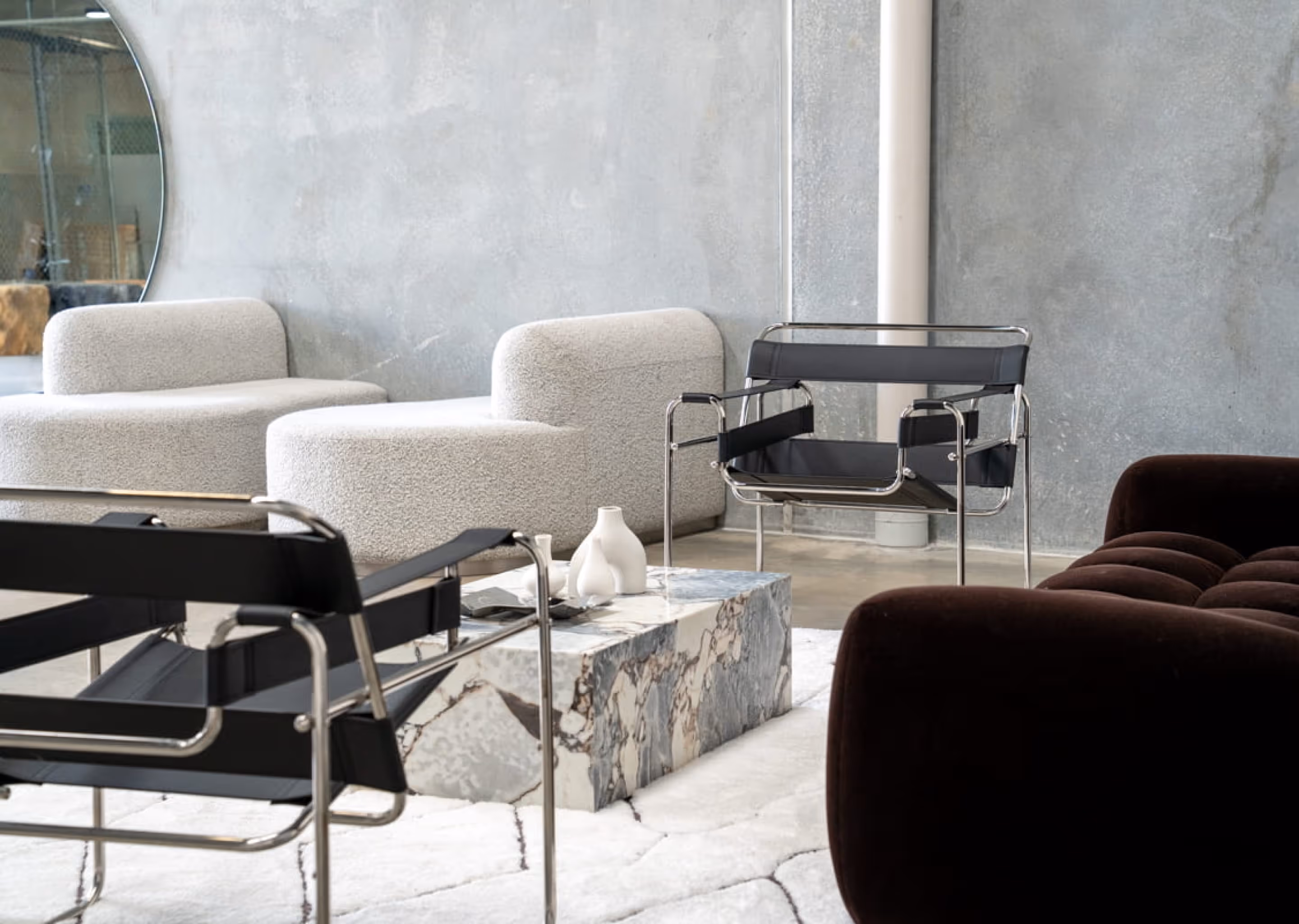 Modern living room with black leather chairs, white textured sofas, marble coffee table, and a round wall mirror.
