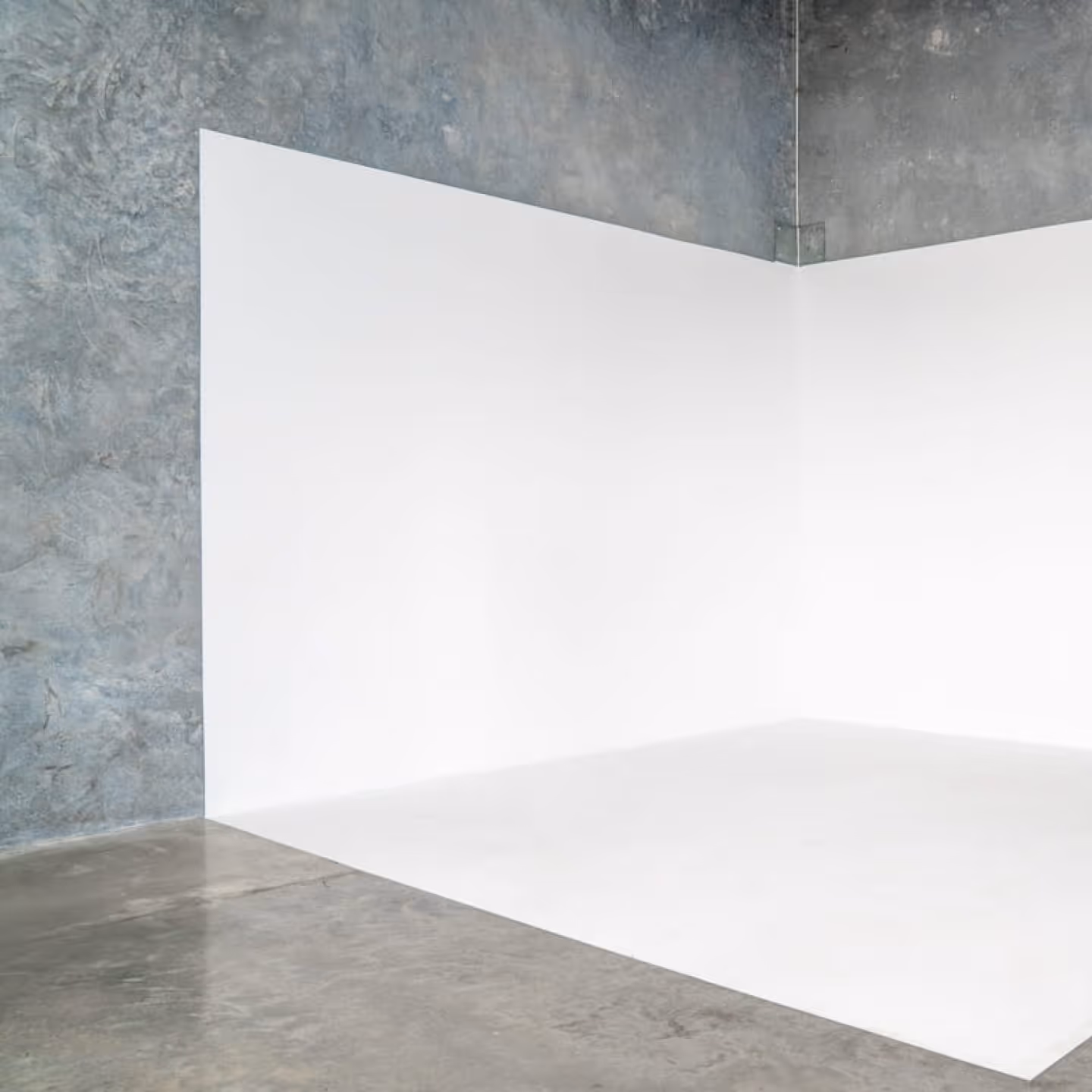 Empty corner with white walls meeting a polished concrete floor and a textured gray wall above.