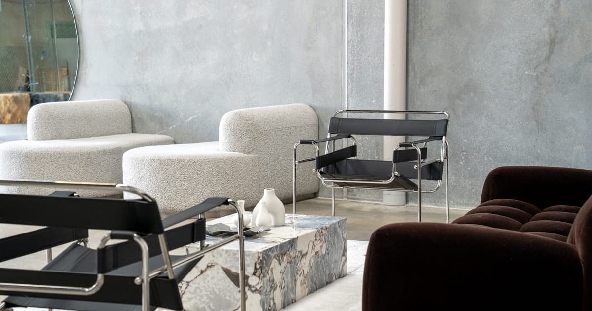 Modern living room with black leather chairs, white textured ottomans, dark sofa, and a marble coffee table.