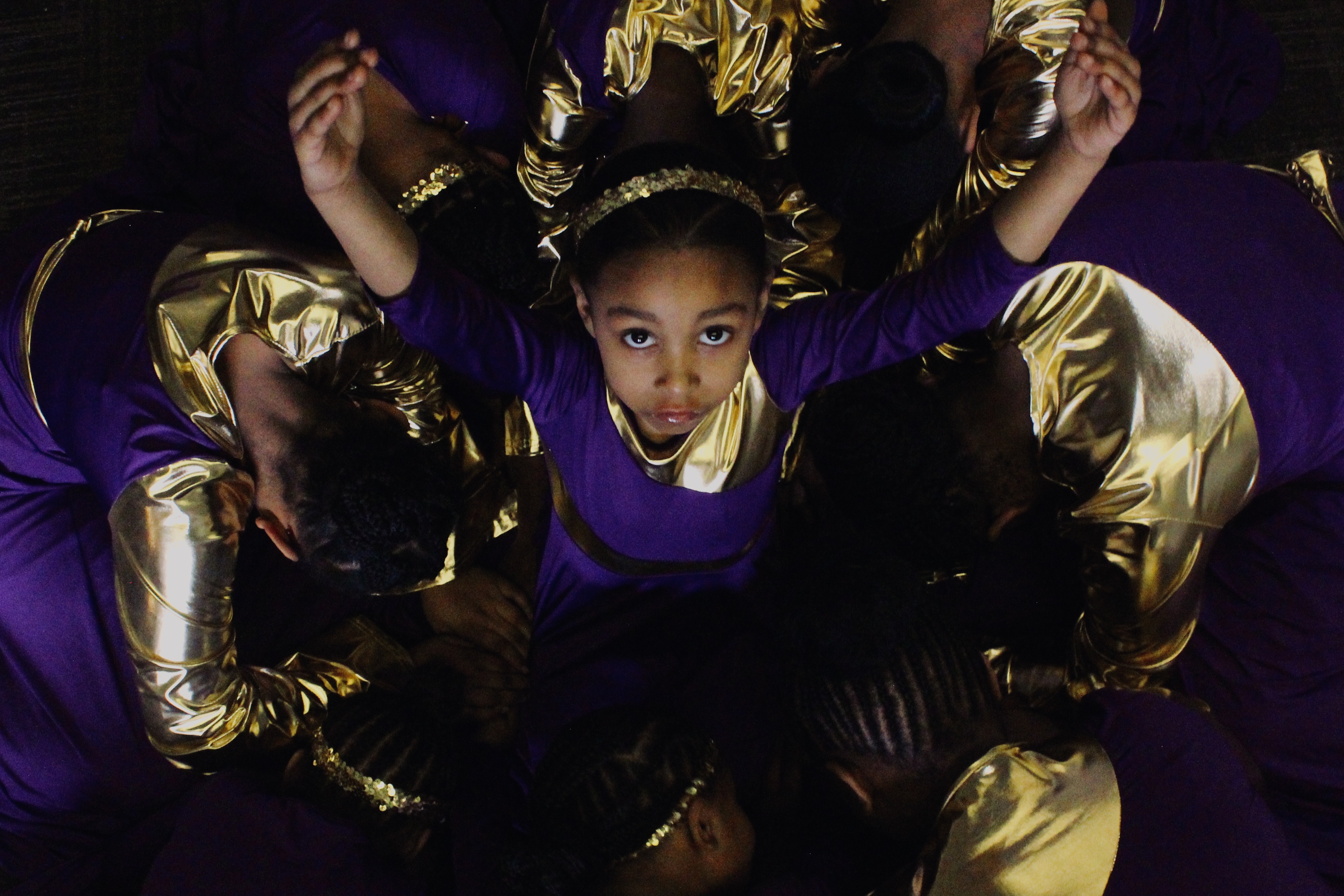 Young, female dance ministers kneel on the floor, surrounding one of their members in a circle.