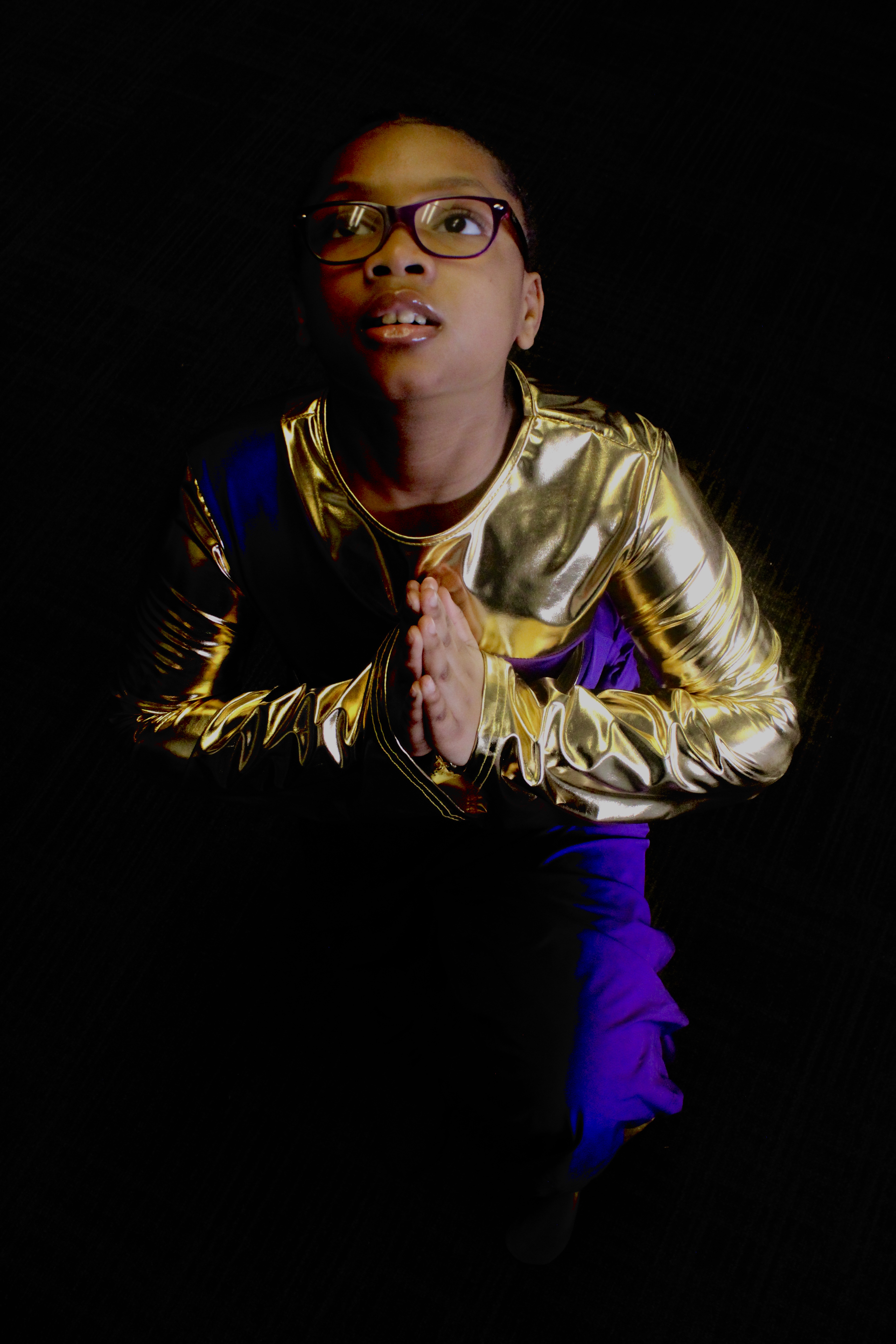 A young, female dance ministers kneels on her knee, looking upward with prayer hands.