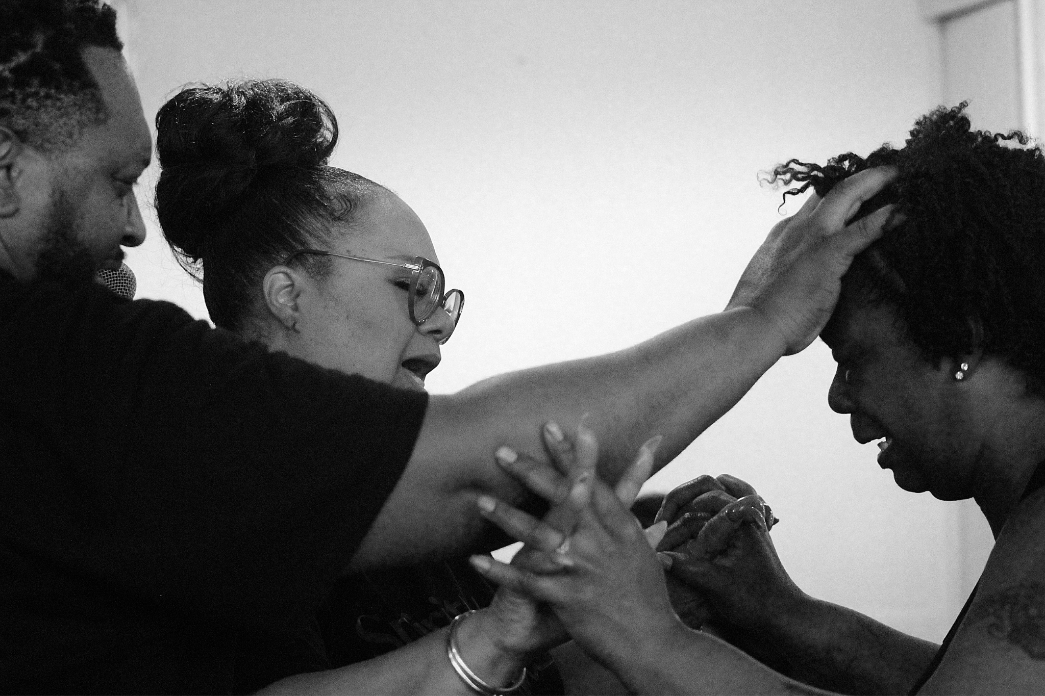 Pastor and Co-Pastor interlock hands with and touch the forehead of a woman being delivered.