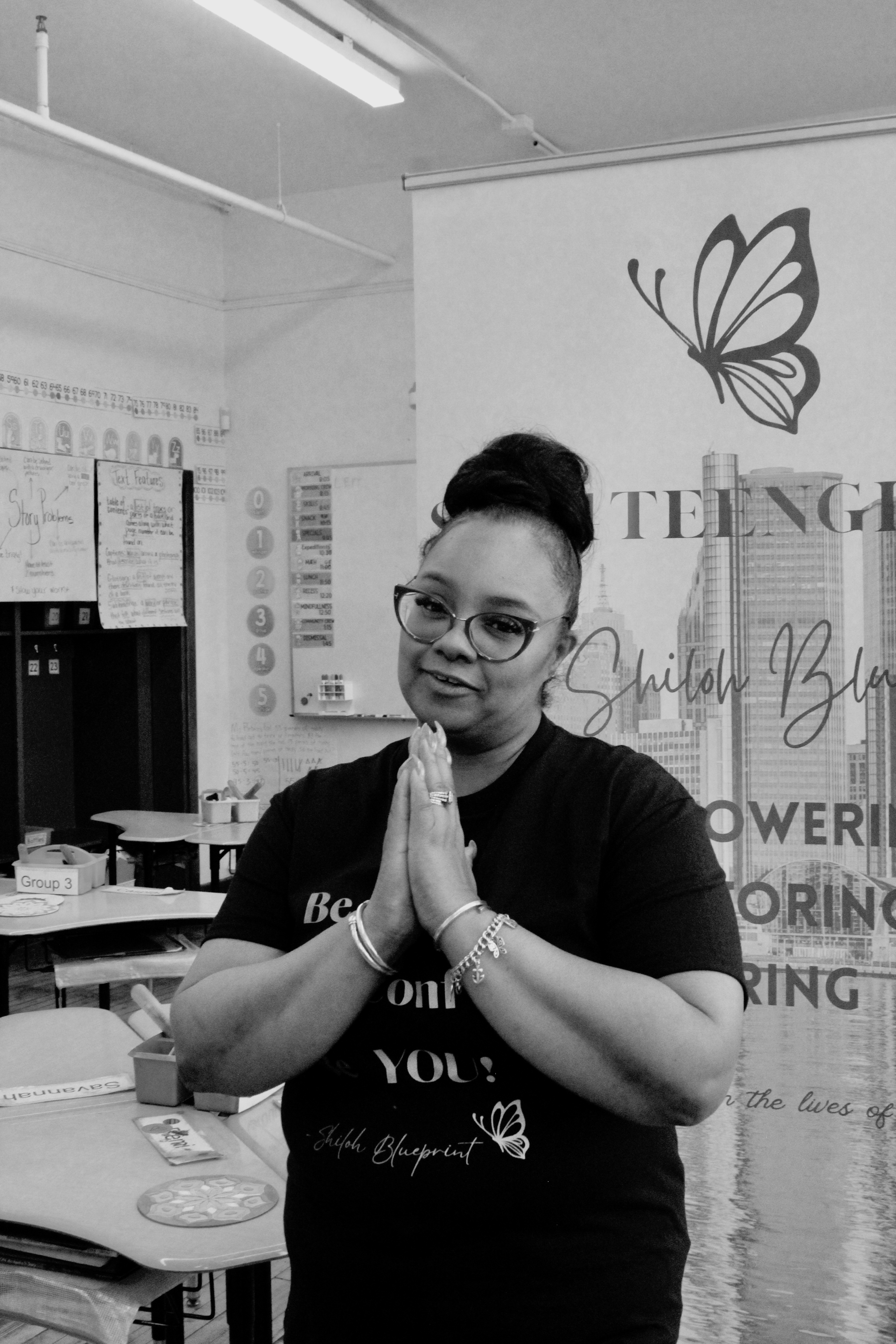 In this black image, Dr. Shalonda thankfully does prayer in front of The Shiloh Blueprint banner. The programs logo, a butterfly, at the top of the banner.