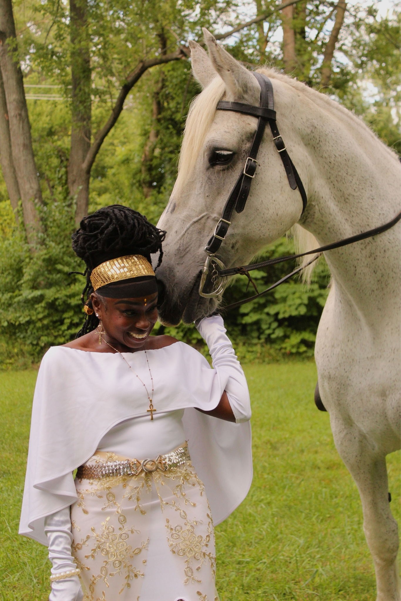 Queen Sabrina stands, smiling like a child as Bell-a grey, female Percheron (horse)-whispers in her ear on a bright, nature-filled, summer day.