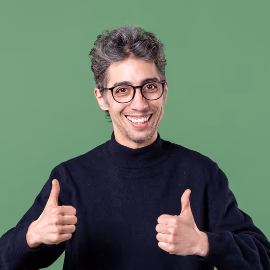 Smiling man with glasses wearing a black sweater giving two thumbs up against a green background.